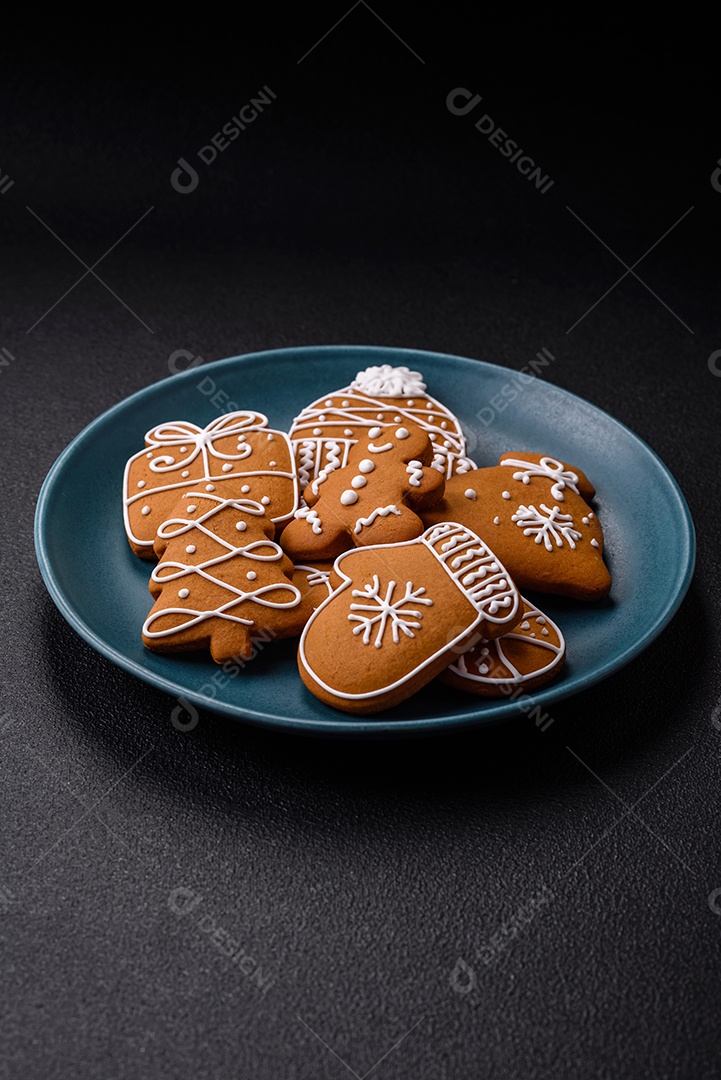 Lindos biscoitos de gengibre de Natal de cores diferentes em uma placa de cerâmica sobre uma mesa de concreto escuro