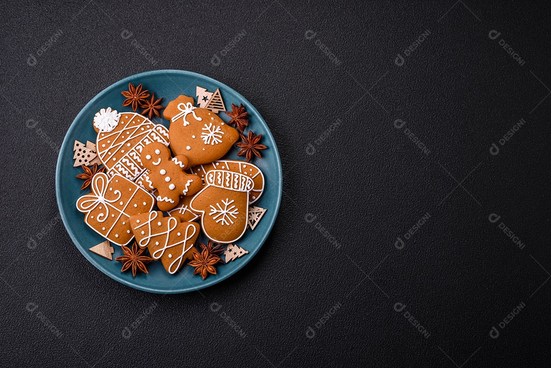 Lindos biscoitos de gengibre de Natal de cores diferentes em uma placa de cerâmica sobre uma mesa de concreto escuro