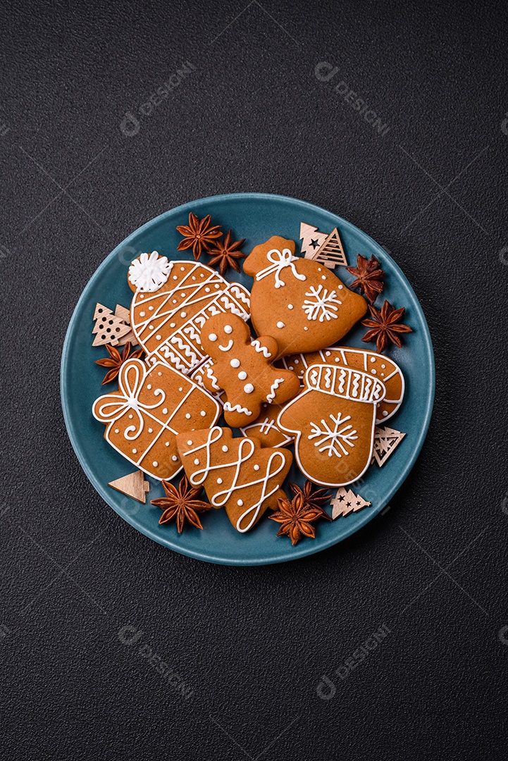 Lindos biscoitos de gengibre de Natal de cores diferentes em uma placa de cerâmica sobre uma mesa de concreto escuro