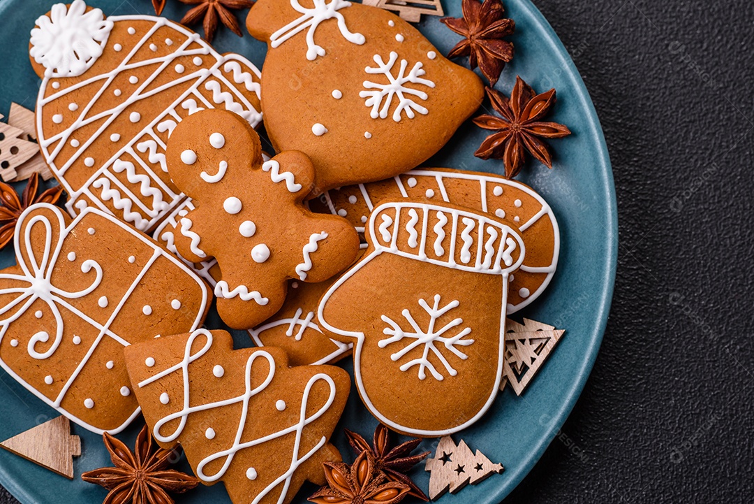 Lindos biscoitos de gengibre de Natal de cores diferentes em uma placa de cerâmica sobre uma mesa de concreto escuro