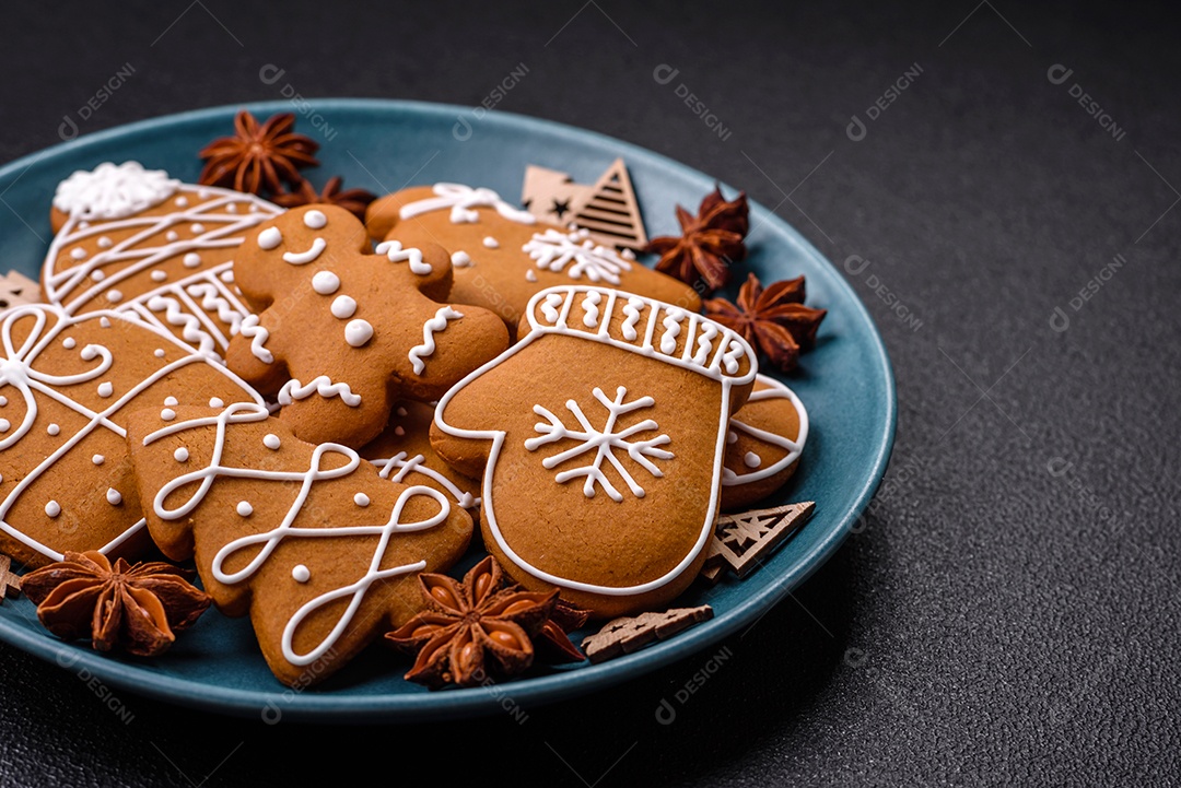 Lindos biscoitos de gengibre de Natal de cores diferentes em uma placa de cerâmica sobre uma mesa de concreto escuro