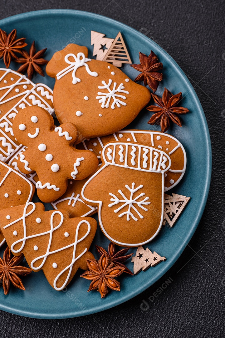 Lindos biscoitos de gengibre de Natal de cores diferentes em uma placa de cerâmica sobre uma mesa de concreto escuro