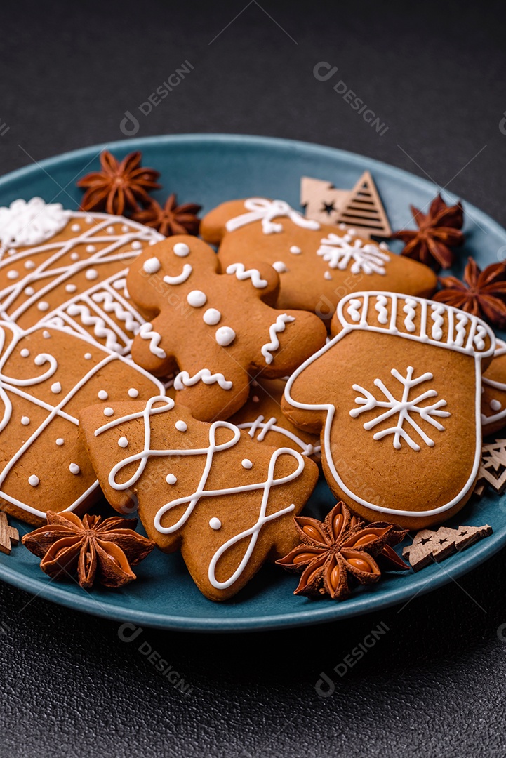 Lindos biscoitos de gengibre de Natal de cores diferentes em uma placa de cerâmica sobre uma mesa de concreto escuro