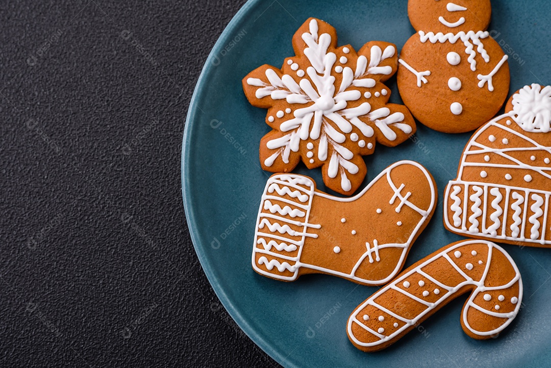 Lindos biscoitos de gengibre de Natal de cores diferentes em uma placa de cerâmica sobre uma mesa de concreto escuro