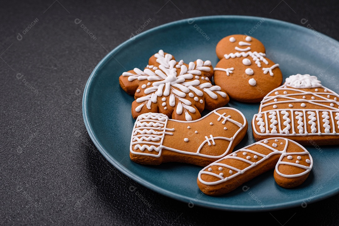 Lindos biscoitos de gengibre de Natal de cores diferentes em uma placa de cerâmica sobre uma mesa de concreto escuro