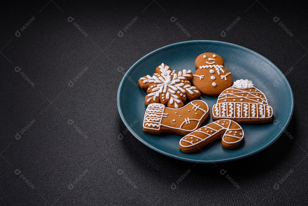 Lindos biscoitos de gengibre de Natal de cores diferentes em uma placa de cerâmica sobre uma mesa de concreto escuro