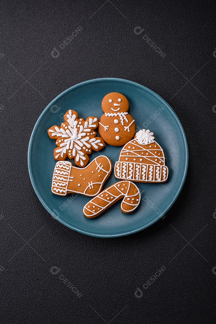 Lindos biscoitos de gengibre de Natal de cores diferentes em uma placa de cerâmica sobre uma mesa de concreto escuro