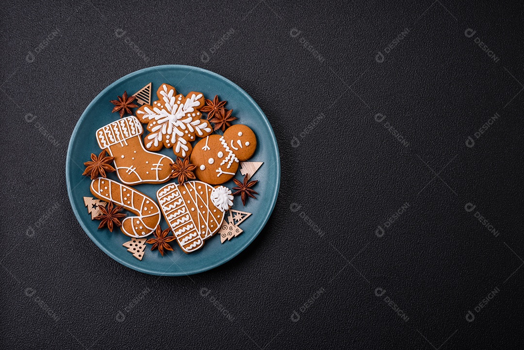 Lindos biscoitos de gengibre de Natal de cores diferentes em uma placa de cerâmica sobre uma mesa de concreto escuro