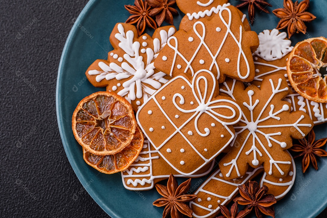 Lindos biscoitos de gengibre de Natal de cores diferentes em uma placa de cerâmica sobre uma mesa de concreto escuro