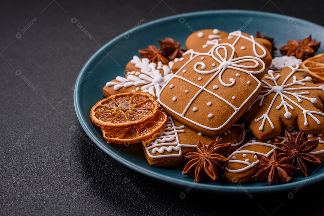 Lindos biscoitos de gengibre de Natal de cores diferentes em uma placa de cerâmica sobre uma mesa de concreto escuro
