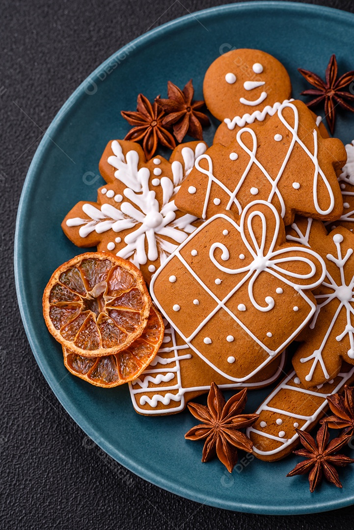 Lindos biscoitos de gengibre de Natal de cores diferentes em uma placa de cerâmica sobre uma mesa de concreto escuro