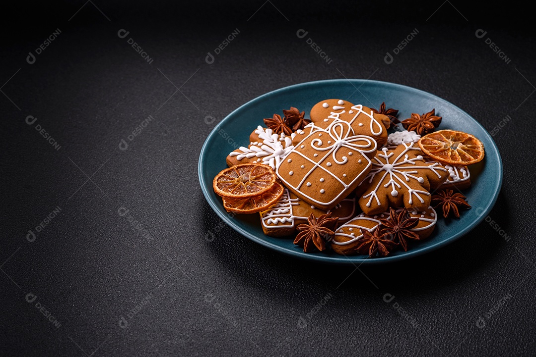 Lindos biscoitos de gengibre de Natal de cores diferentes em uma placa de cerâmica sobre uma mesa de concreto escuro