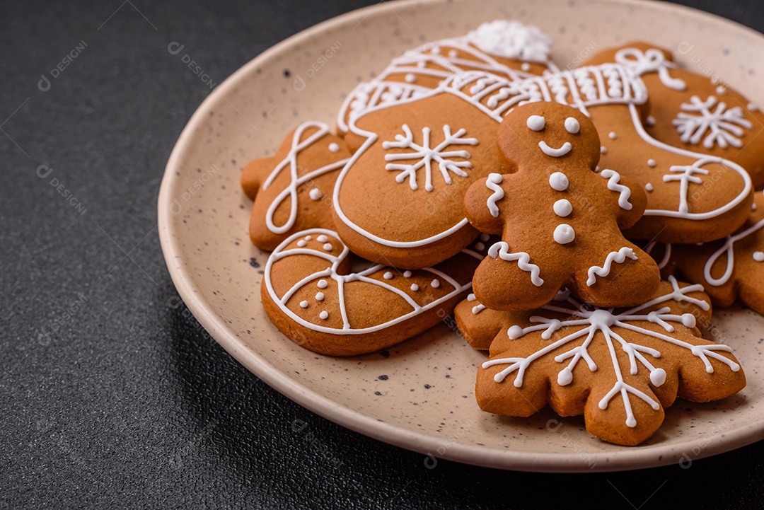 Lindos biscoitos de gengibre de Natal de cores diferentes em uma placa de cerâmica sobre uma mesa de concreto escuro
