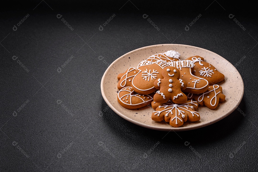 Lindos biscoitos de gengibre de Natal de cores diferentes em uma placa de cerâmica sobre uma mesa de concreto escuro