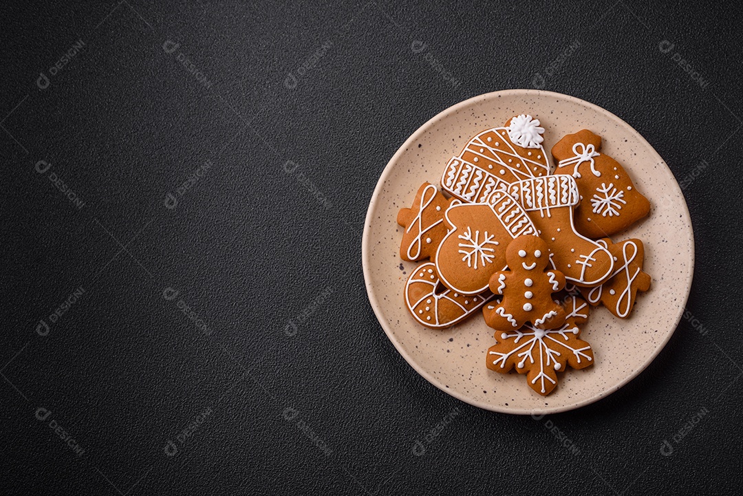 Lindos biscoitos de gengibre de Natal de cores diferentes em uma placa de cerâmica sobre uma mesa de concreto escuro