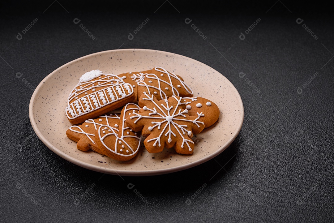 Lindos biscoitos de gengibre de Natal de cores diferentes em uma placa de cerâmica sobre uma mesa de concreto escuro