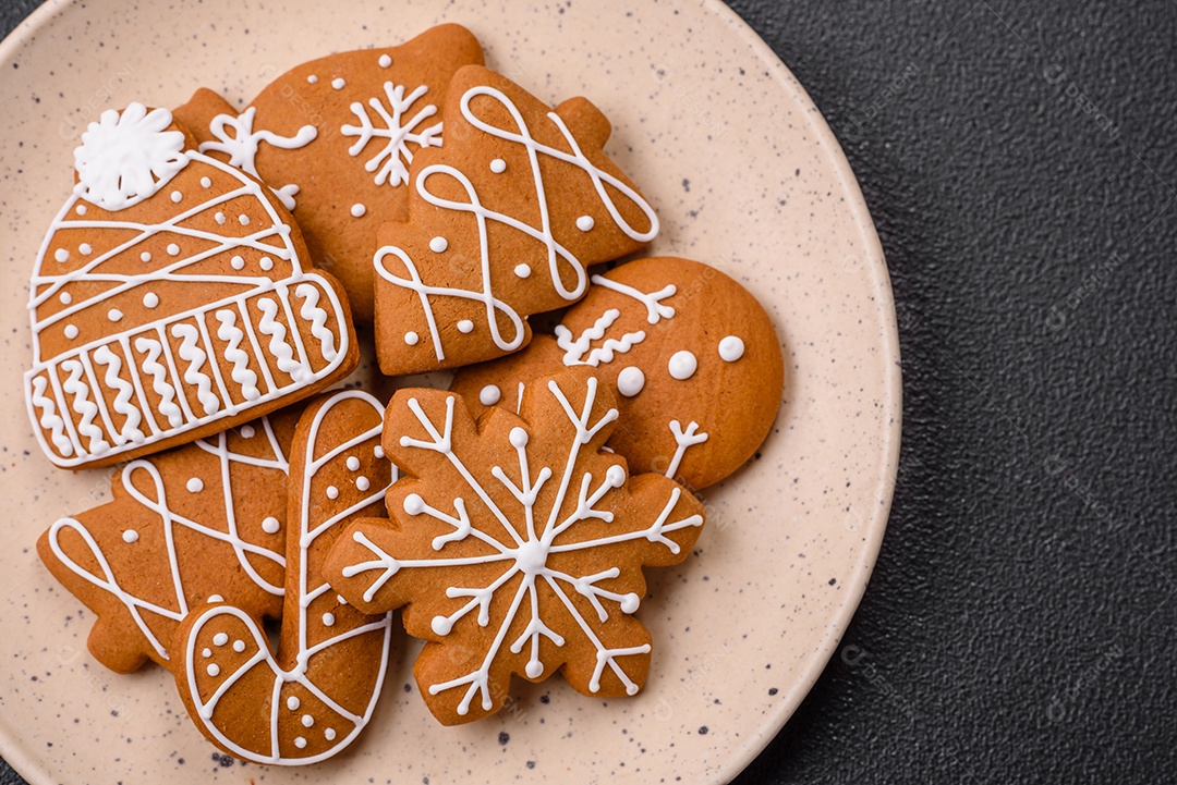 Lindos biscoitos de gengibre de Natal de cores diferentes em uma placa de cerâmica sobre uma mesa de concreto escuro