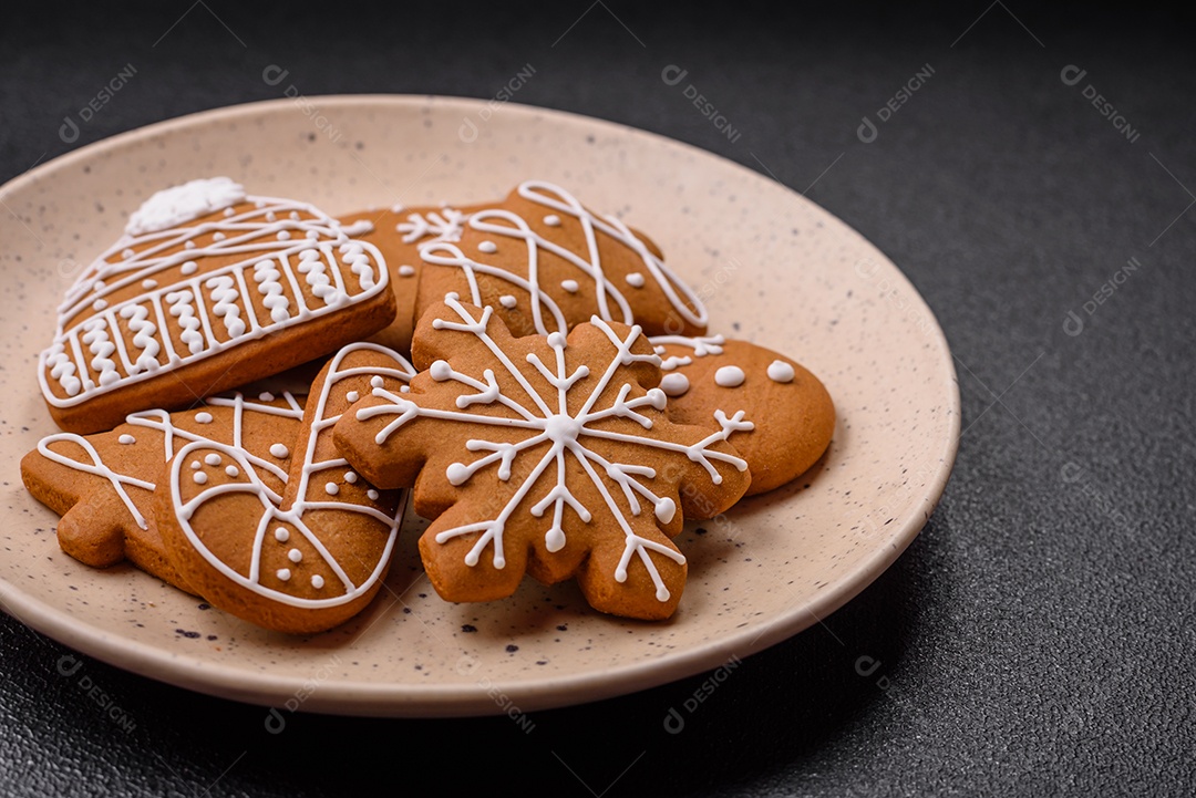 Lindos biscoitos de gengibre de Natal de cores diferentes em uma placa de cerâmica sobre uma mesa de concreto escuro