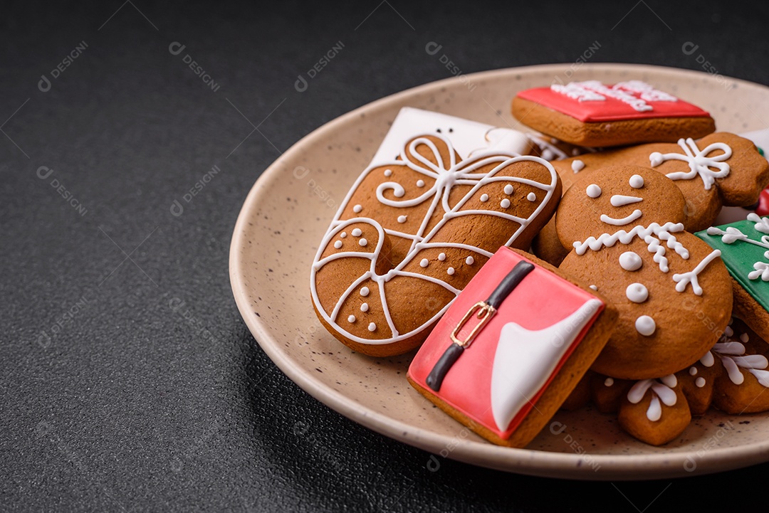 Lindos biscoitos de gengibre de Natal de cores diferentes em uma placa de cerâmica sobre uma mesa de concreto escuro