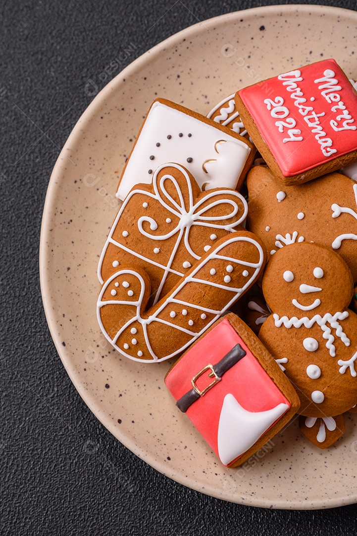 Lindos biscoitos de gengibre de Natal de cores diferentes em uma placa de cerâmica sobre uma mesa de concreto escuro