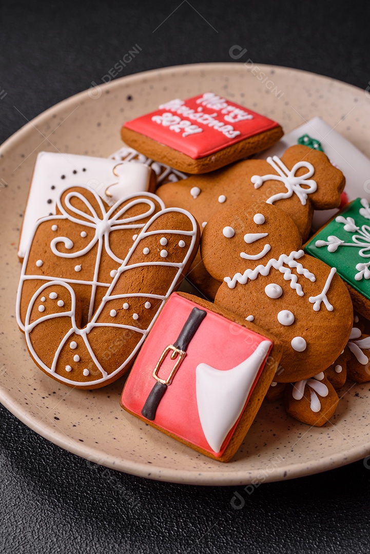 Lindos biscoitos de gengibre de Natal de cores diferentes em uma placa de cerâmica sobre uma mesa de concreto escuro