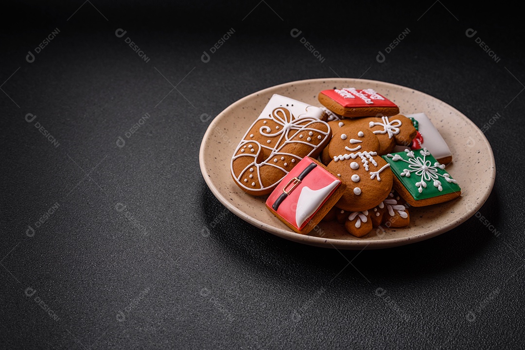 Lindos biscoitos de gengibre de Natal de cores diferentes em uma placa de cerâmica sobre uma mesa de concreto escuro