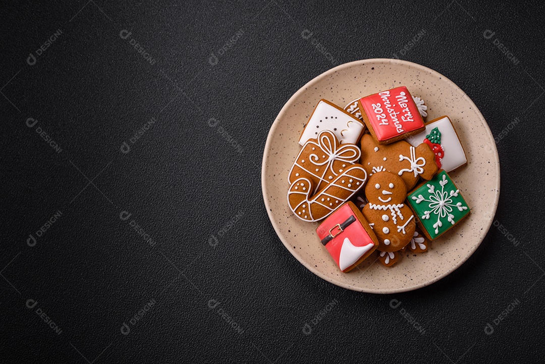 Lindos biscoitos de gengibre de Natal de cores diferentes em uma placa de cerâmica sobre uma mesa de concreto escuro