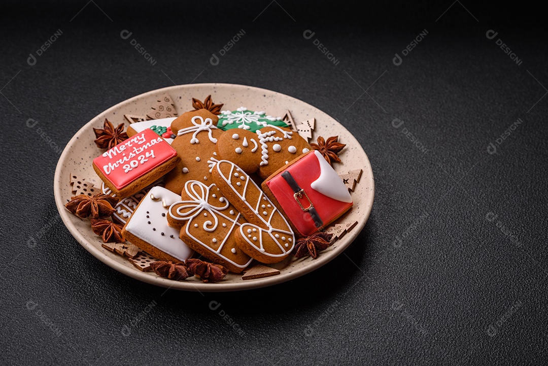 Lindos biscoitos de gengibre de Natal de cores diferentes em uma placa de cerâmica sobre uma mesa de concreto escuro