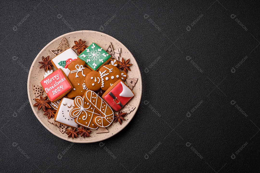 Lindos biscoitos de gengibre de Natal de cores diferentes em uma placa de cerâmica sobre uma mesa de concreto escuro