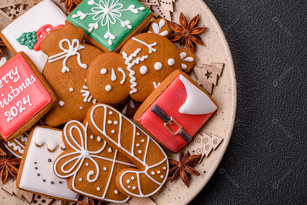 Lindos biscoitos de gengibre de Natal de cores diferentes em uma placa de cerâmica sobre uma mesa de concreto escuro