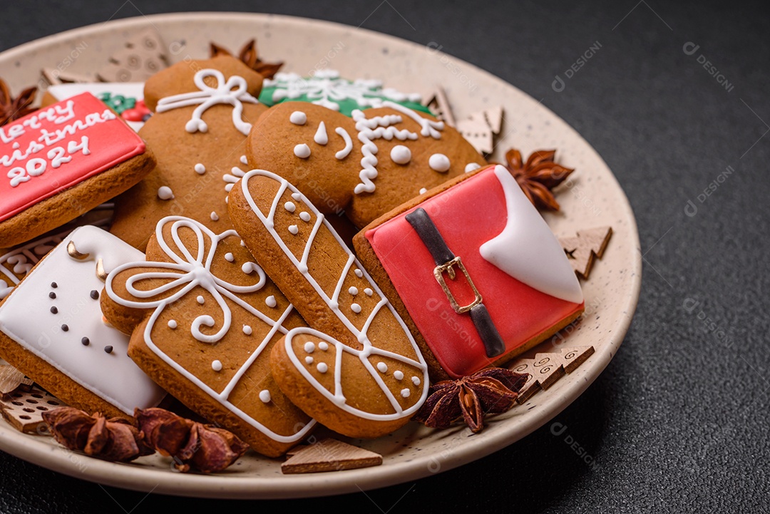 Lindos biscoitos de gengibre de Natal de cores diferentes em uma placa de cerâmica sobre uma mesa de concreto escuro