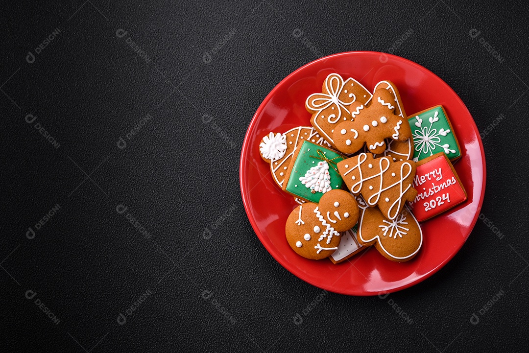 Lindos biscoitos de gengibre de Natal de cores diferentes em uma placa de cerâmica sobre uma mesa de concreto escuro