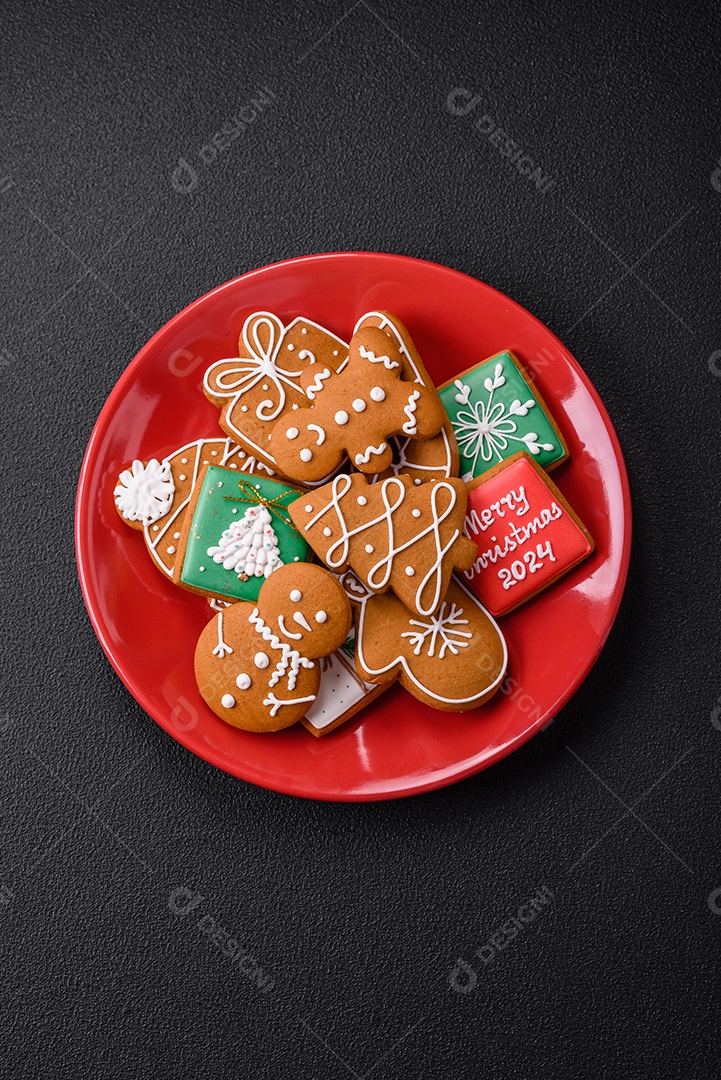 Lindos biscoitos de gengibre de Natal de cores diferentes em uma placa de cerâmica sobre uma mesa de concreto escuro