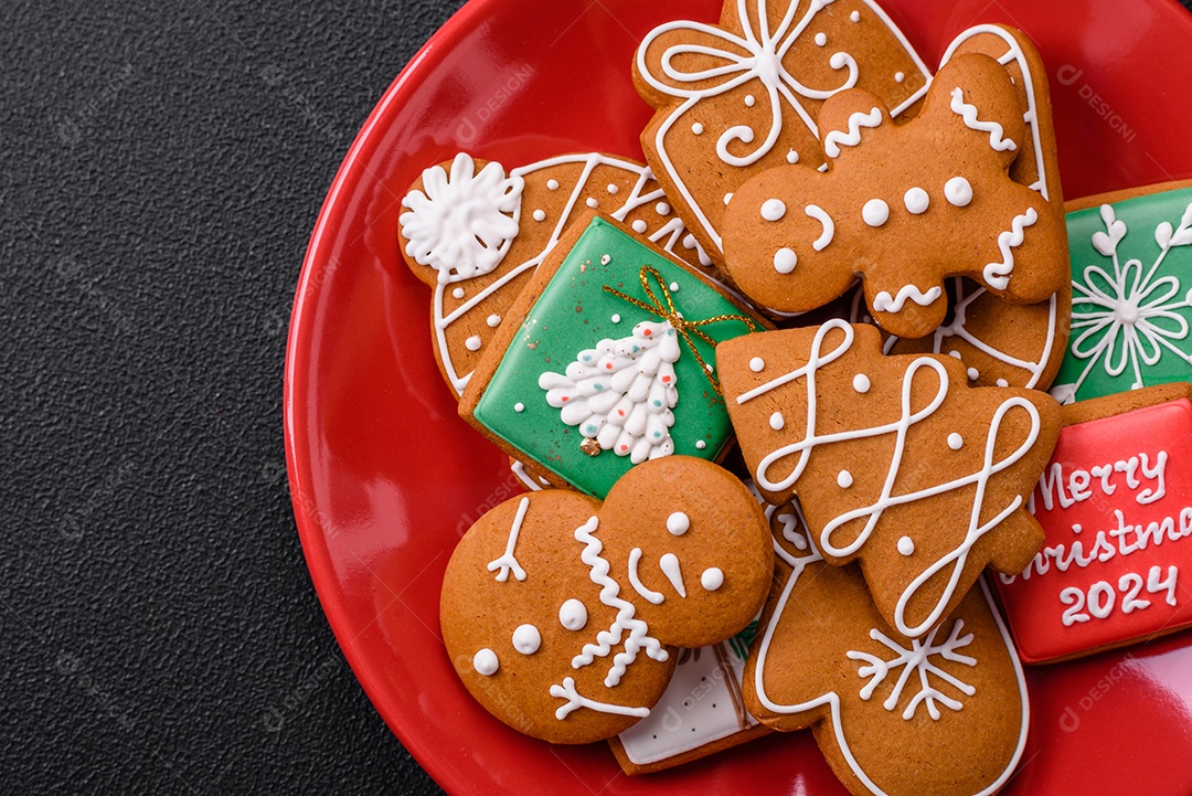 Lindos biscoitos de gengibre de Natal de cores diferentes em uma placa de cerâmica sobre uma mesa de concreto escuro