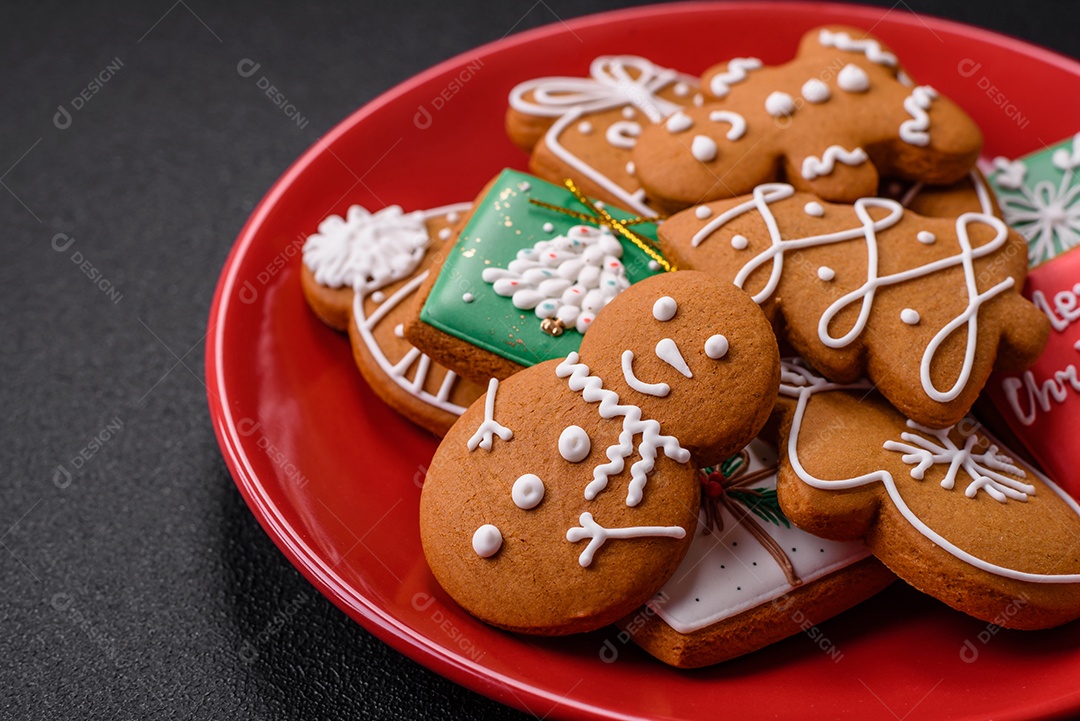 Lindos biscoitos de gengibre de Natal de cores diferentes em uma placa de cerâmica sobre uma mesa de concreto escuro