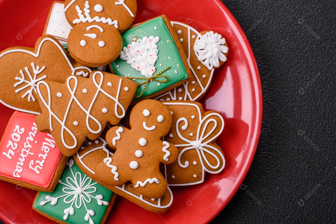 Lindos biscoitos de gengibre de Natal de cores diferentes em uma placa de cerâmica sobre uma mesa de concreto escuro