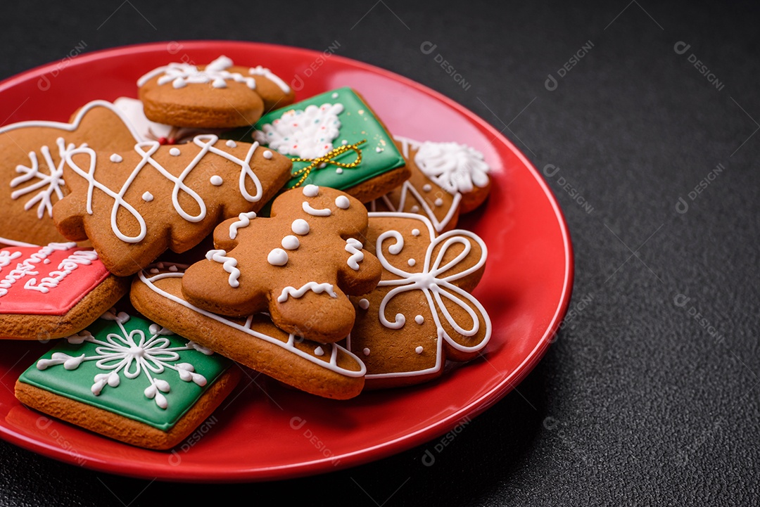 Lindos biscoitos de gengibre de Natal de cores diferentes em uma placa de cerâmica sobre uma mesa de concreto escuro