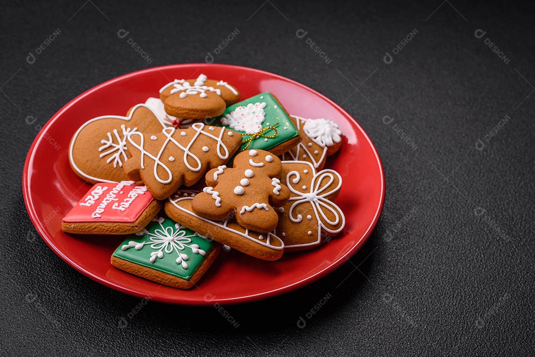 Lindos biscoitos de gengibre de Natal de cores diferentes em uma placa de cerâmica sobre uma mesa de concreto escuro