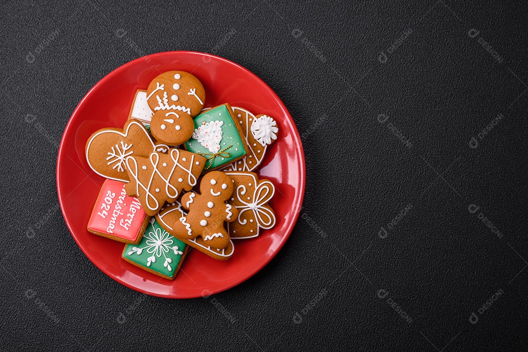 Lindos biscoitos de gengibre de Natal de cores diferentes em uma placa de cerâmica sobre uma mesa de concreto escuro