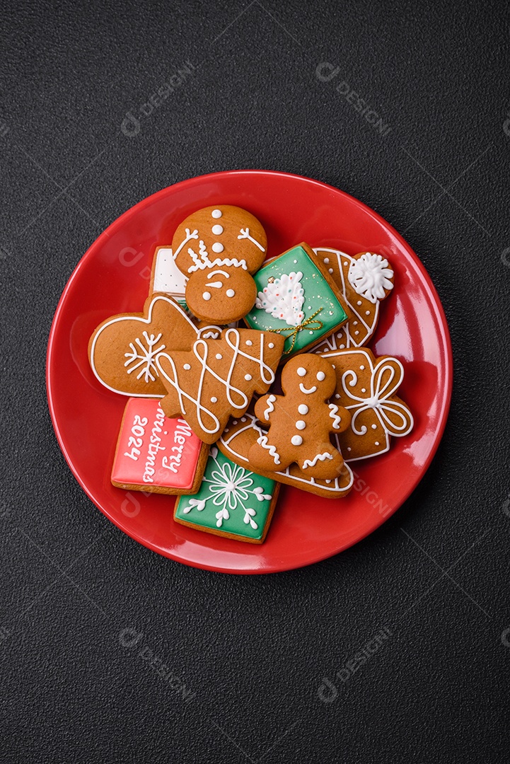 Lindos biscoitos de gengibre de Natal de cores diferentes em uma placa de cerâmica sobre uma mesa de concreto escur