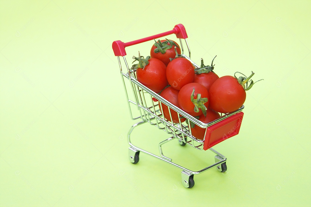 Mini carrinho de compra com tomates cerejas sobre fundo verde