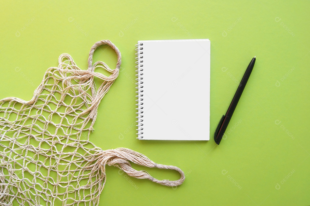 Sacola reutilizável de barbante com caderno e caneta sobre fundo verde