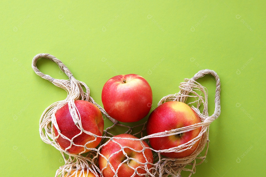 Saco de barbante com maçãs dentro sobre fundo verde