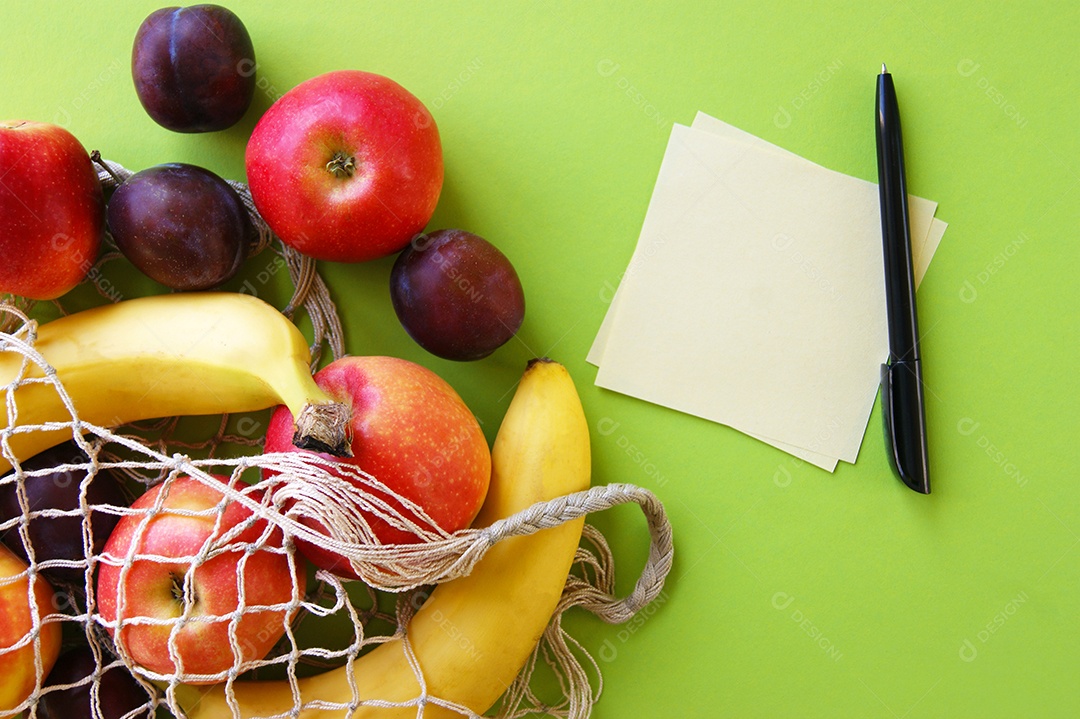 Frutas sobre uma mesa com papel e caneta ao lado sobre fundo verde
