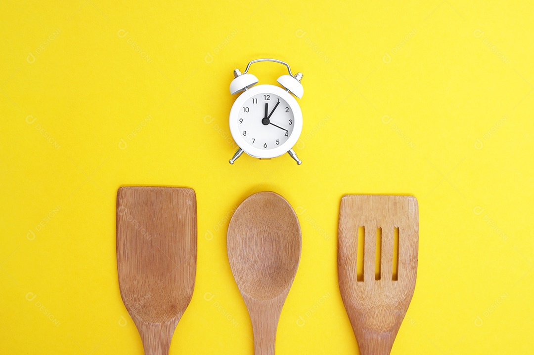 Colheres grande de bambu para cozinha e um relógio branco sobre fundo amarelo