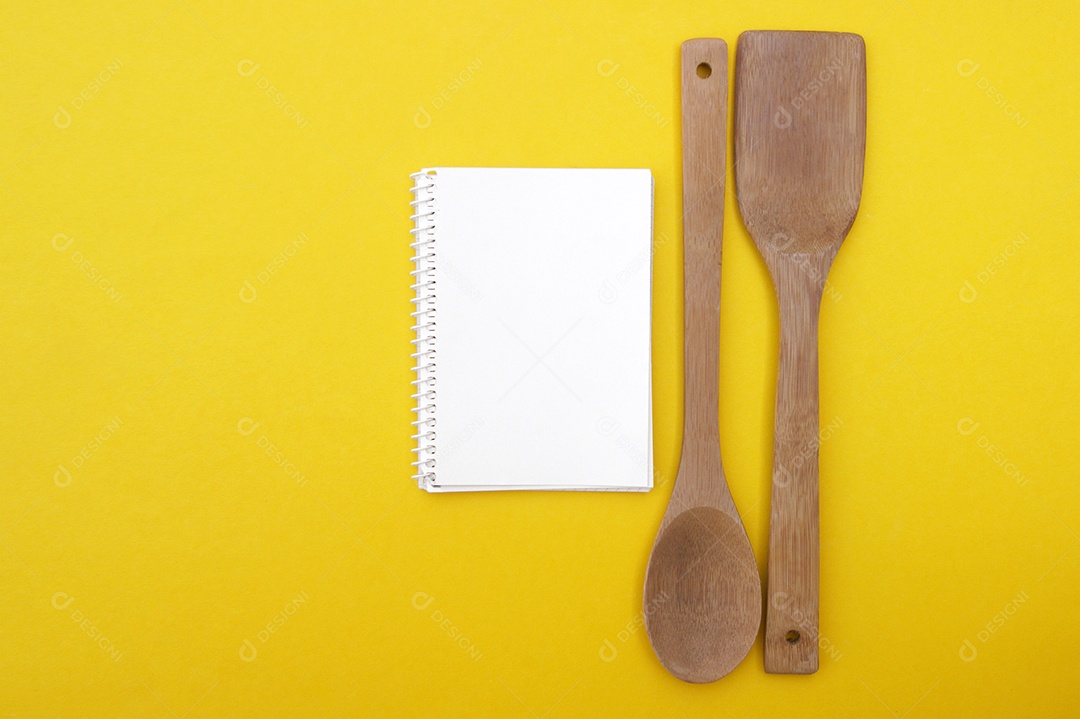 Um conjunto de colheres de bambu e caderno em branco sobre um fundo amarelo