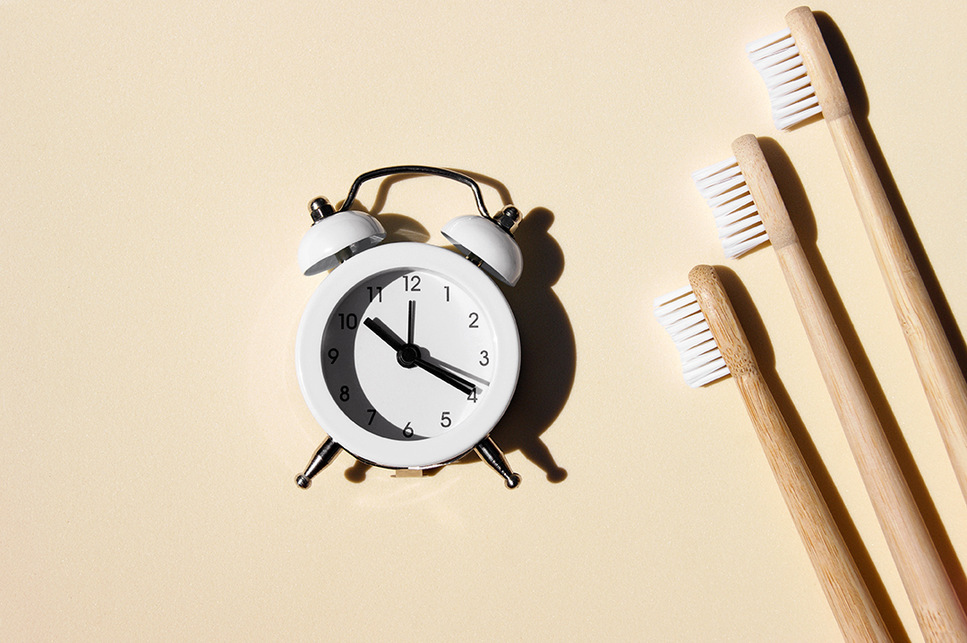 Escovas de dente de bambu lindas e relógio branco sobre fundo claro