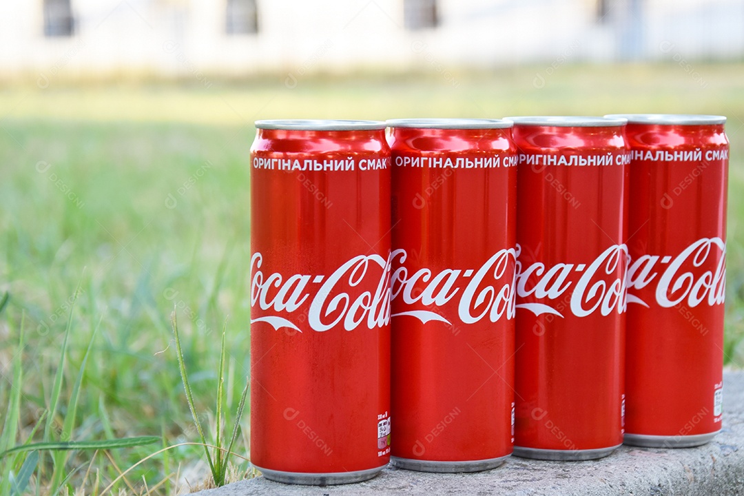 Quatro latas de coca cola sobre fundo gramado