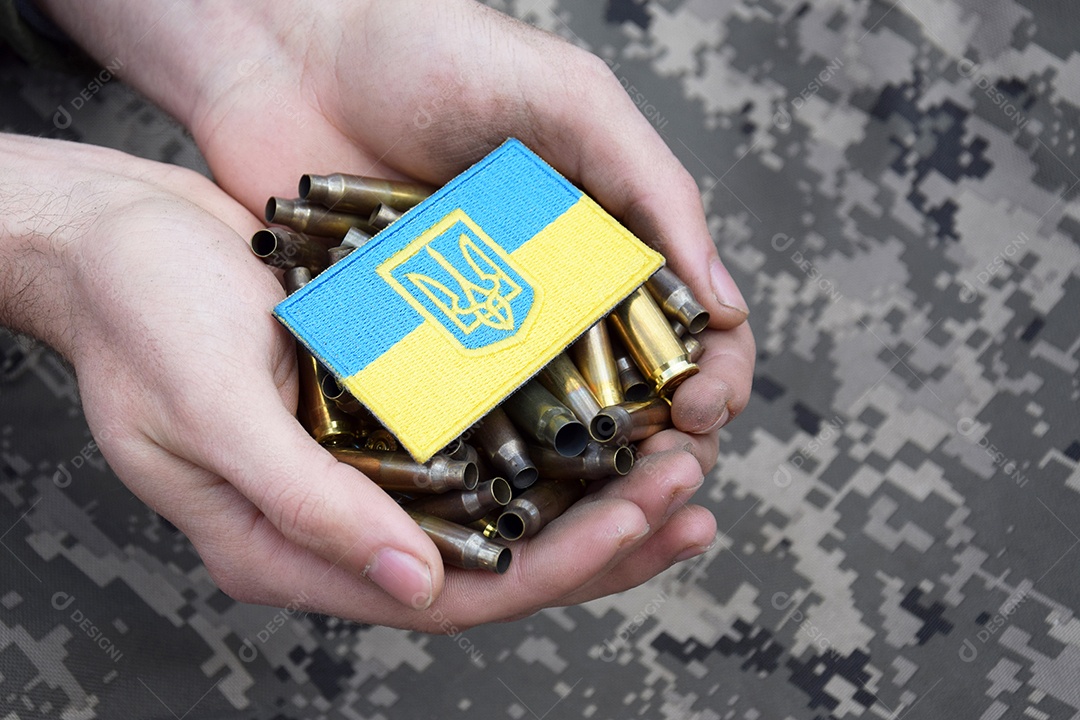 Mãos segurando muitos cartuchos e bandeira da Ucrânia em meio a guerra