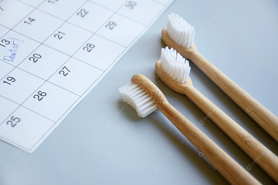 Três escovas de dentes de bambu e calendário sobre fundo cinza